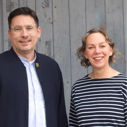Ein Mann und eine Frau lachend vor einer Wand